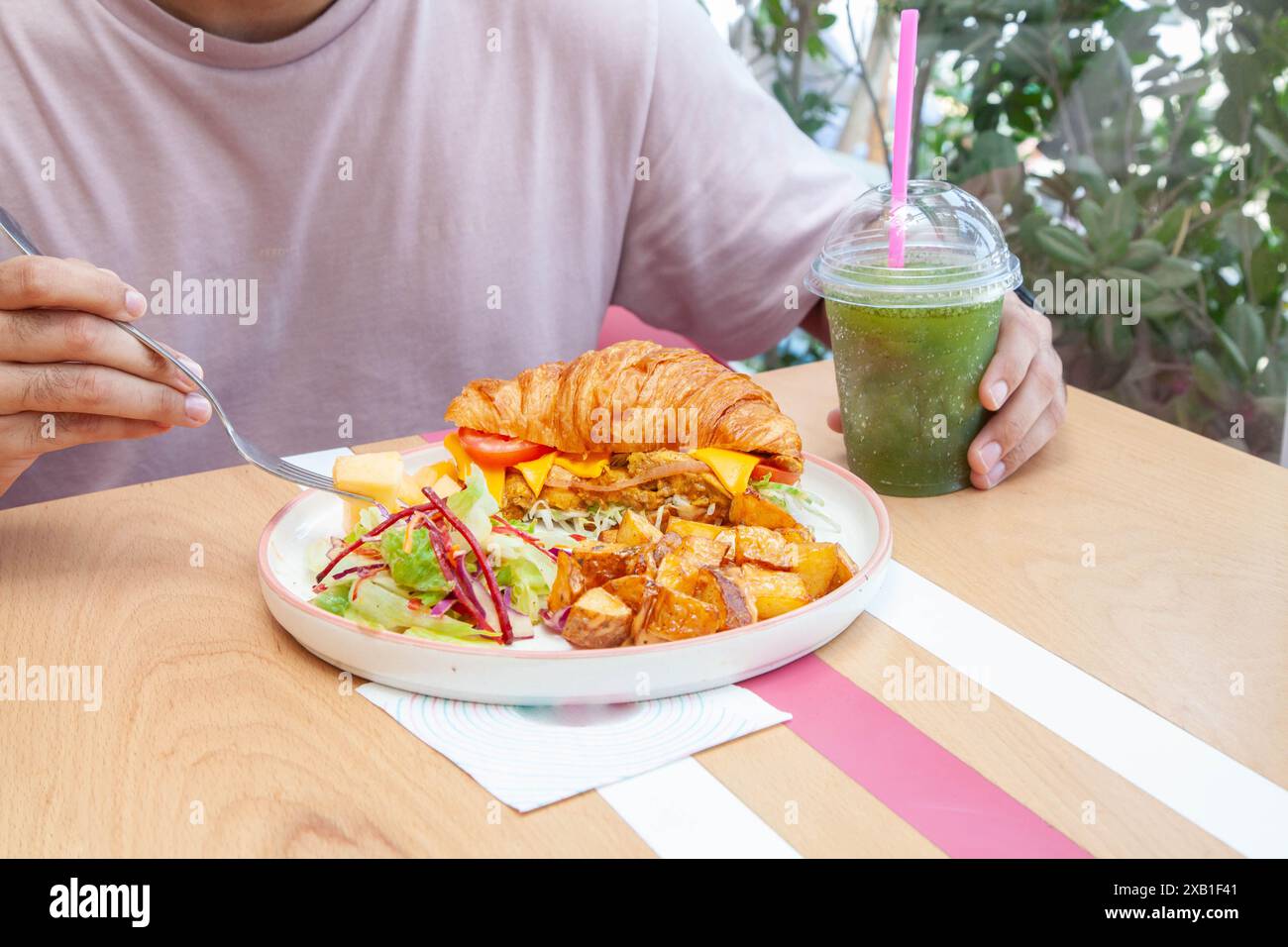 Homme mangeant un sandwich croissants brioche avec une boisson à la limonade à la menthe dans un café. Banque D'Images