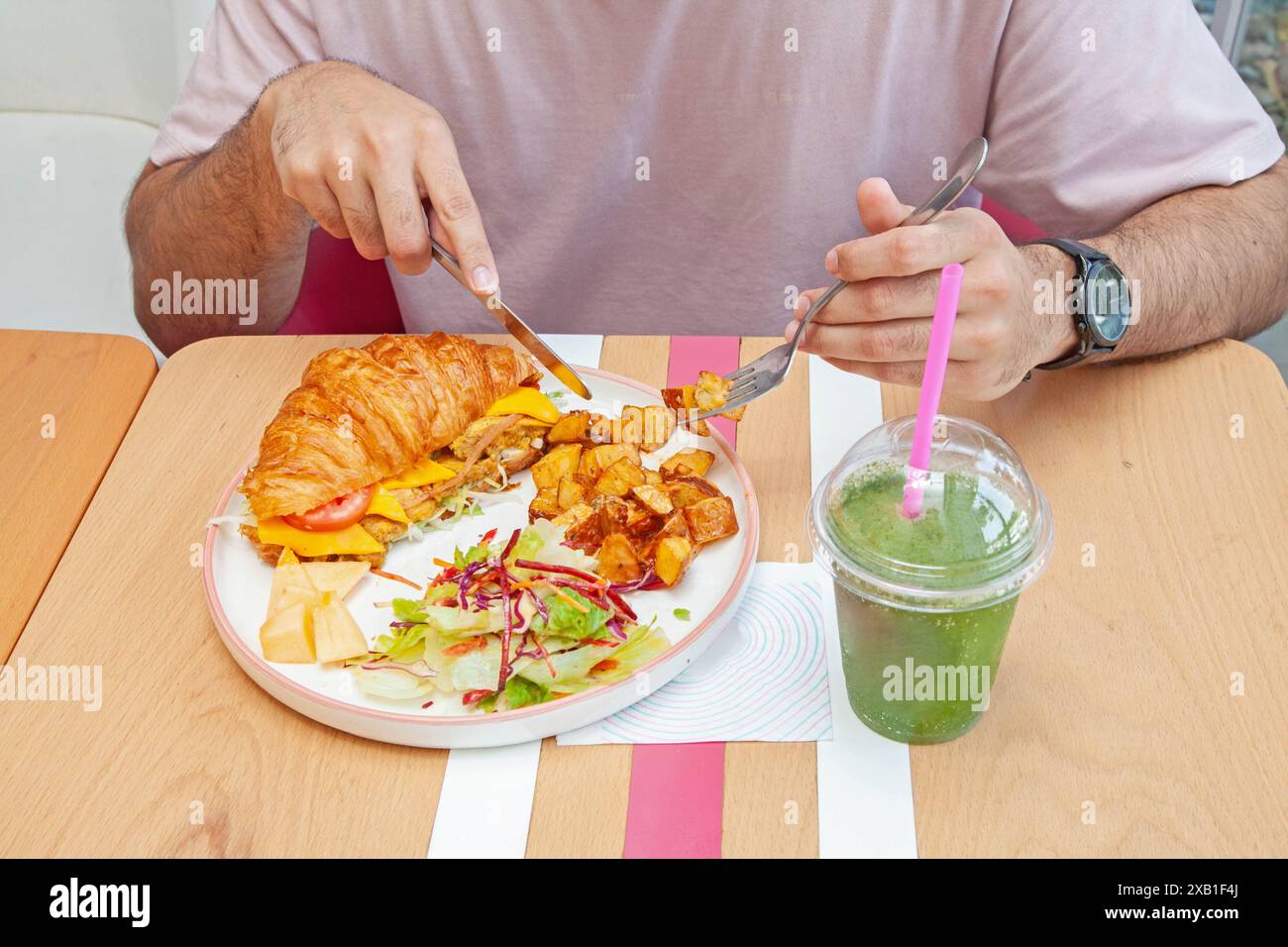 Homme mangeant un sandwich croissants brioche avec une boisson à la limonade à la menthe dans un café. Banque D'Images