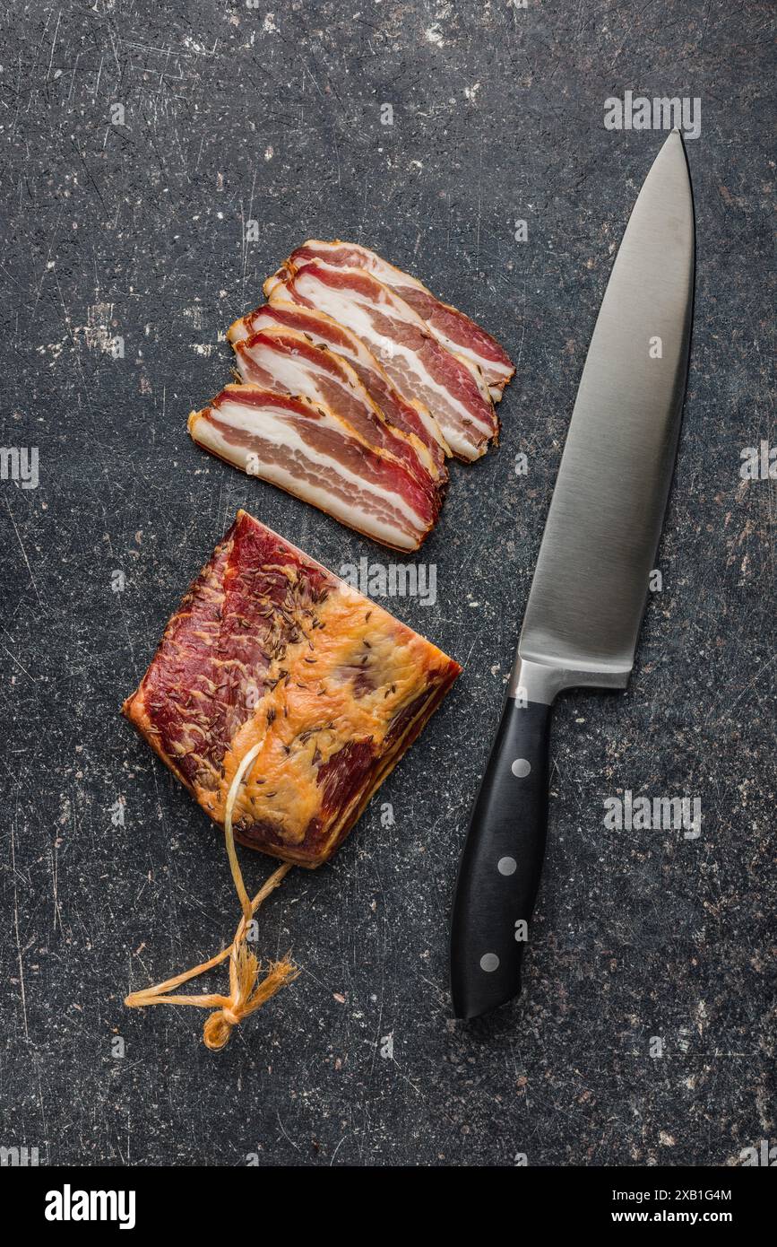 Gros plan de tranches de bacon fumé et couteau sur une table noire. Vue de dessus. Banque D'Images