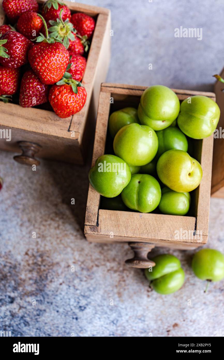 Fraises mûres biologiques, cerises douces et prunes vertes disposées dans des boîtes en bois vintage sur une surface texturée, mettant en valeur la richesse colorée de la nature Banque D'Images