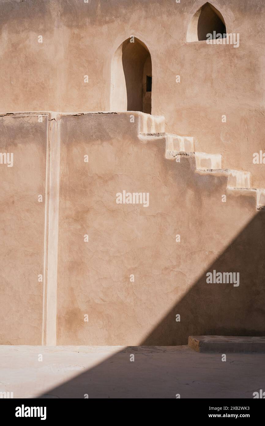 Une composition minimaliste d'un bâtiment omanais traditionnel en adobe, avec un escalier et une porte voûtée, capturant l'essence de l'architecture d'Oman Banque D'Images