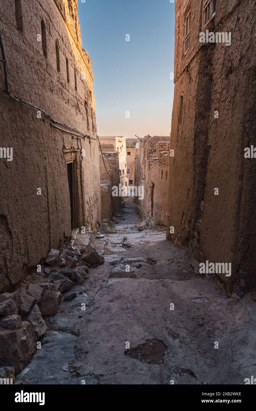 Une ruelle altérée passe entre les maisons traditionnelles en brique de boue dans un vieux village omanais, capturant l'essence de l'Oman rural pendant un coucher de soleil doré Banque D'Images
