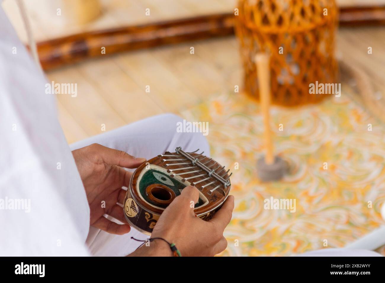 Mains d'une personne anonyme recadrée jouant d'une kalimba, un instrument africain traditionnel, lors d'une séance de thérapie sonore, avec un gong flou dans le b. Banque D'Images