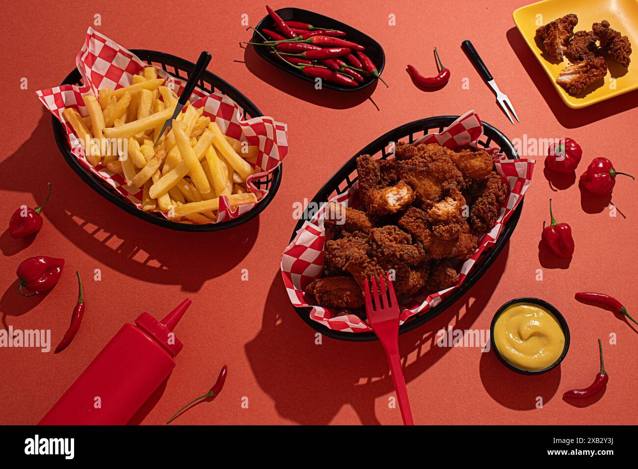 Un délicieux arrangement de poulet frit croustillant et de frites dorées servies dans des paniers noirs avec des doublures à carreaux rouges et blancs, entourés de rouge frais Banque D'Images