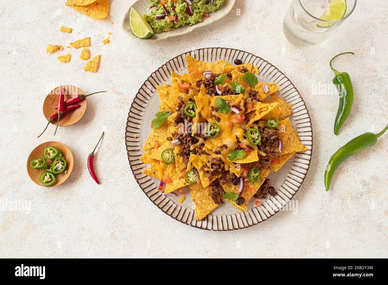 Vue de dessus d'une assiette salée de nachos empilés haut avec du bœuf, du guacamole, du fromage fondu, des jalapenos et des garnitures fraîches servies avec du citron vert et du rafraîchissement Banque D'Images