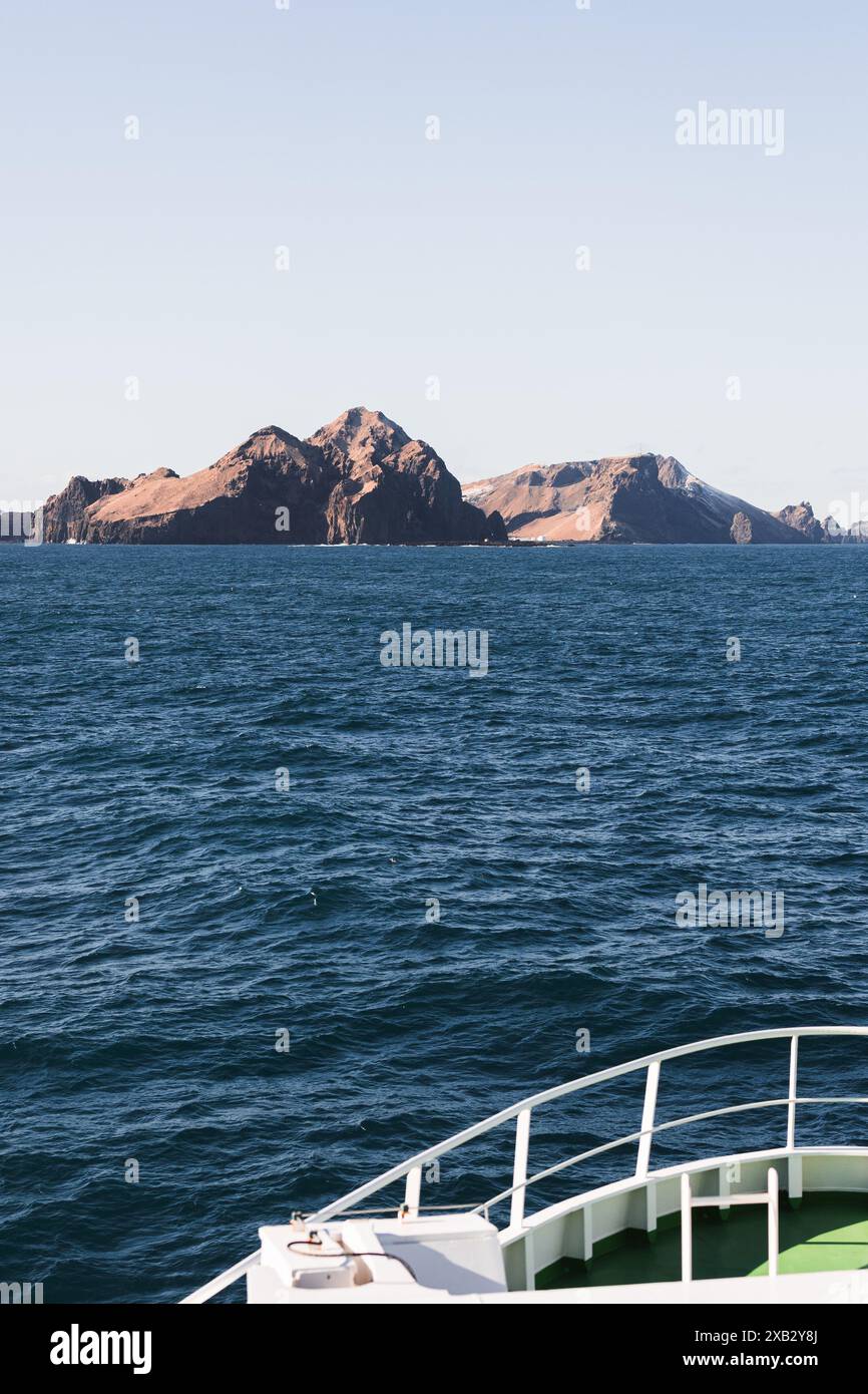 Vue depuis un bateau montrant l'étendue sereine de l'océan menant aux falaises escarpées des îles Westman, sous un ciel dégagé Banque D'Images