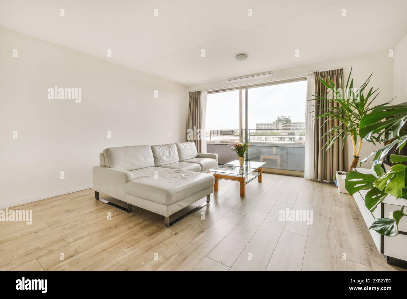 Appartement lumineux et spacieux avec un élégant canapé en cuir blanc, parquet, et un balcon joliment orné avec vue sur le paysage urbain, situé i Banque D'Images