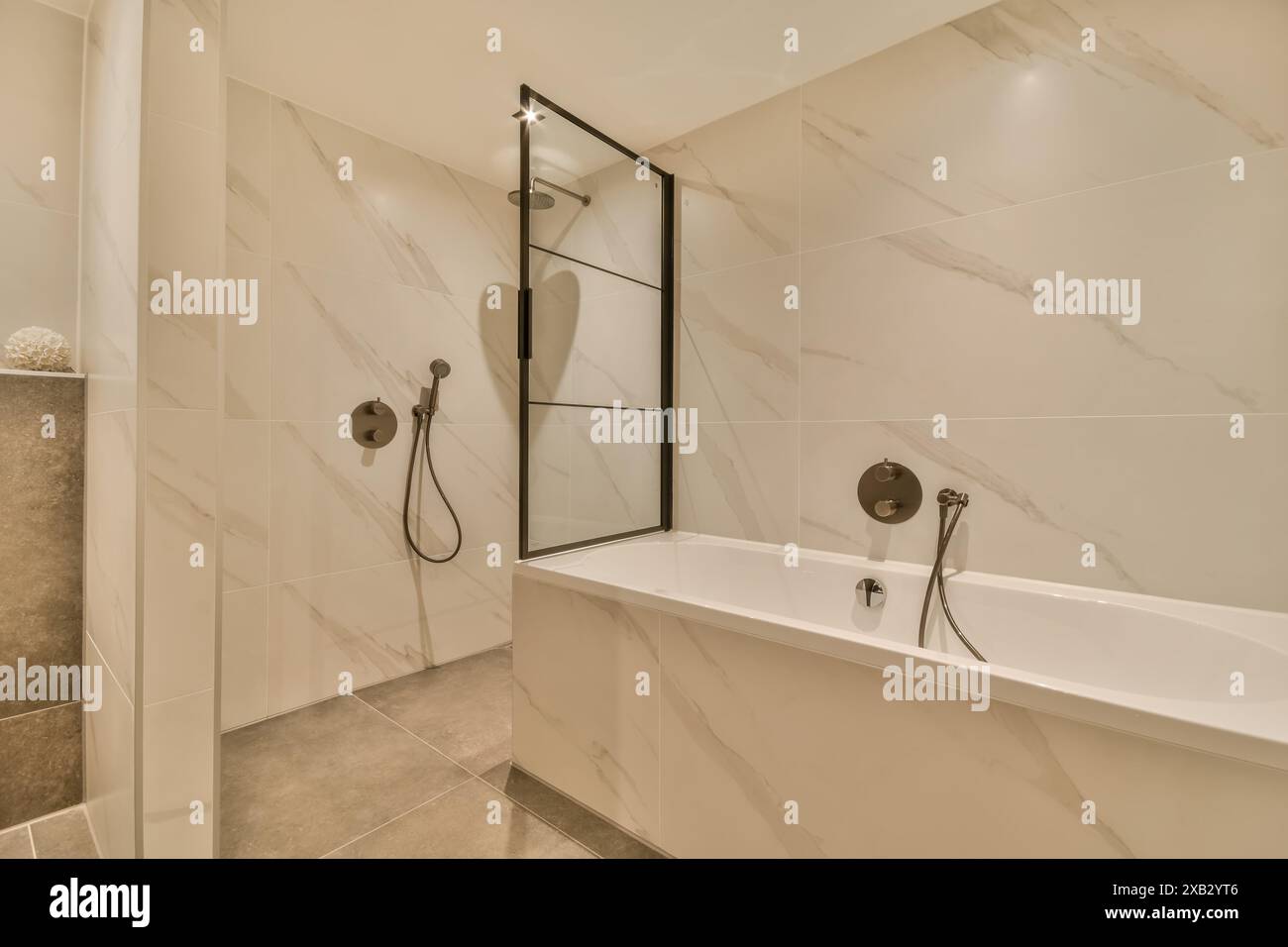 Cette élégante salle de bains contemporaine est décorée de carreaux muraux en marbre poli, d'une cabine de douche en verre, de luminaires élégants et d'une baignoire blanche. Banque D'Images