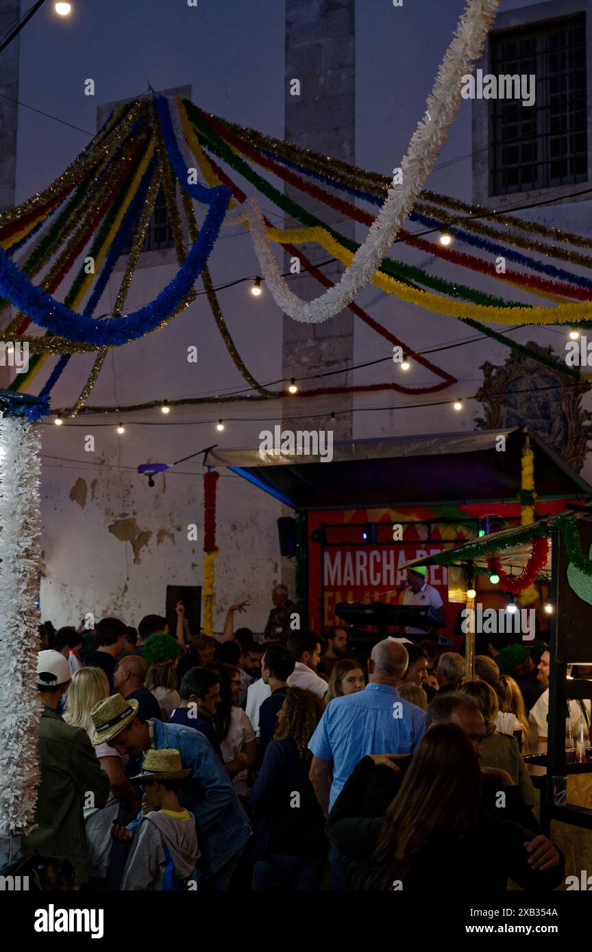 Alfama pendant les festivités populaires des saints, des banderoles colorées se drapent sur la place, créant une canopée vibrante au-dessus de la foule dansante Banque D'Images