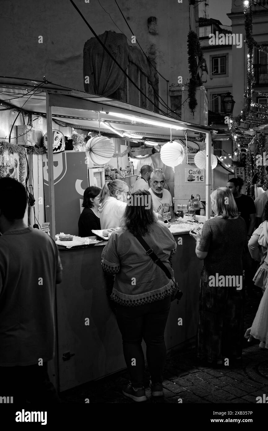 Les gens se rassemblent à un stand de nourriture et de boisson très éclairé décoré de lanternes en papier colorées pendant les festivités populaires des Saints à Alfama Banque D'Images