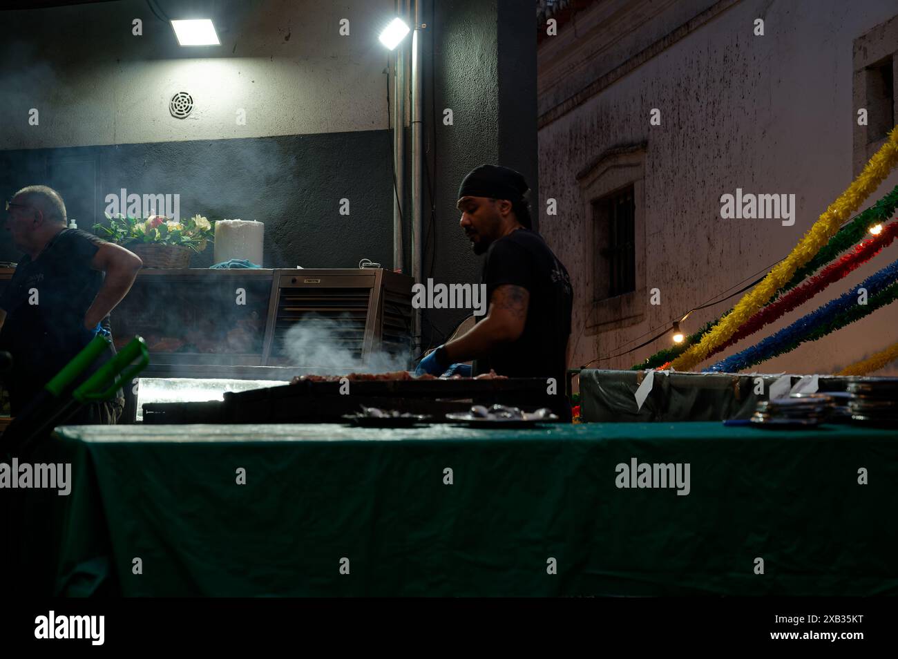 Le vendeur grillera de la nourriture dans un étal de rue pendant les festivités populaires des Saints à Alfama, avec un lever de fumée et des décorations colorées qui ajoutent à la scène Banque D'Images