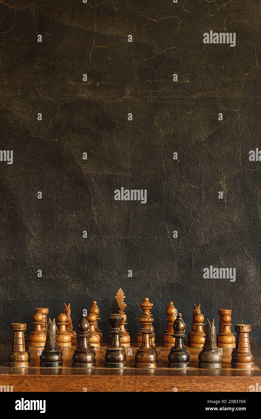 Pièces antiques de jeu d'échecs en bois vieilli devant un fond noir texturé Banque D'Images