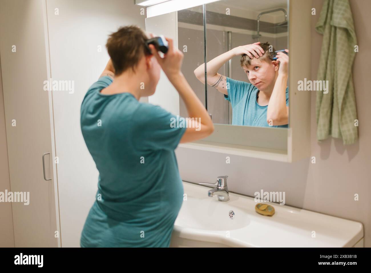 Jeune femme enceinte taillant les cheveux devant le miroir à la salle de bain Banque D'Images