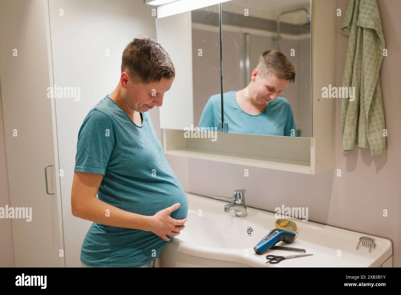 Jeune femme enceinte touchant l'abdomen par la tondeuse à cheveux devant le miroir à la salle de bain Banque D'Images