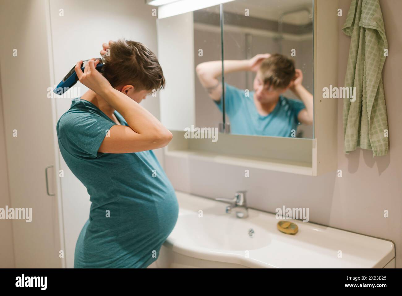 Femme enceinte taillant les cheveux devant le miroir à la salle de bain Banque D'Images