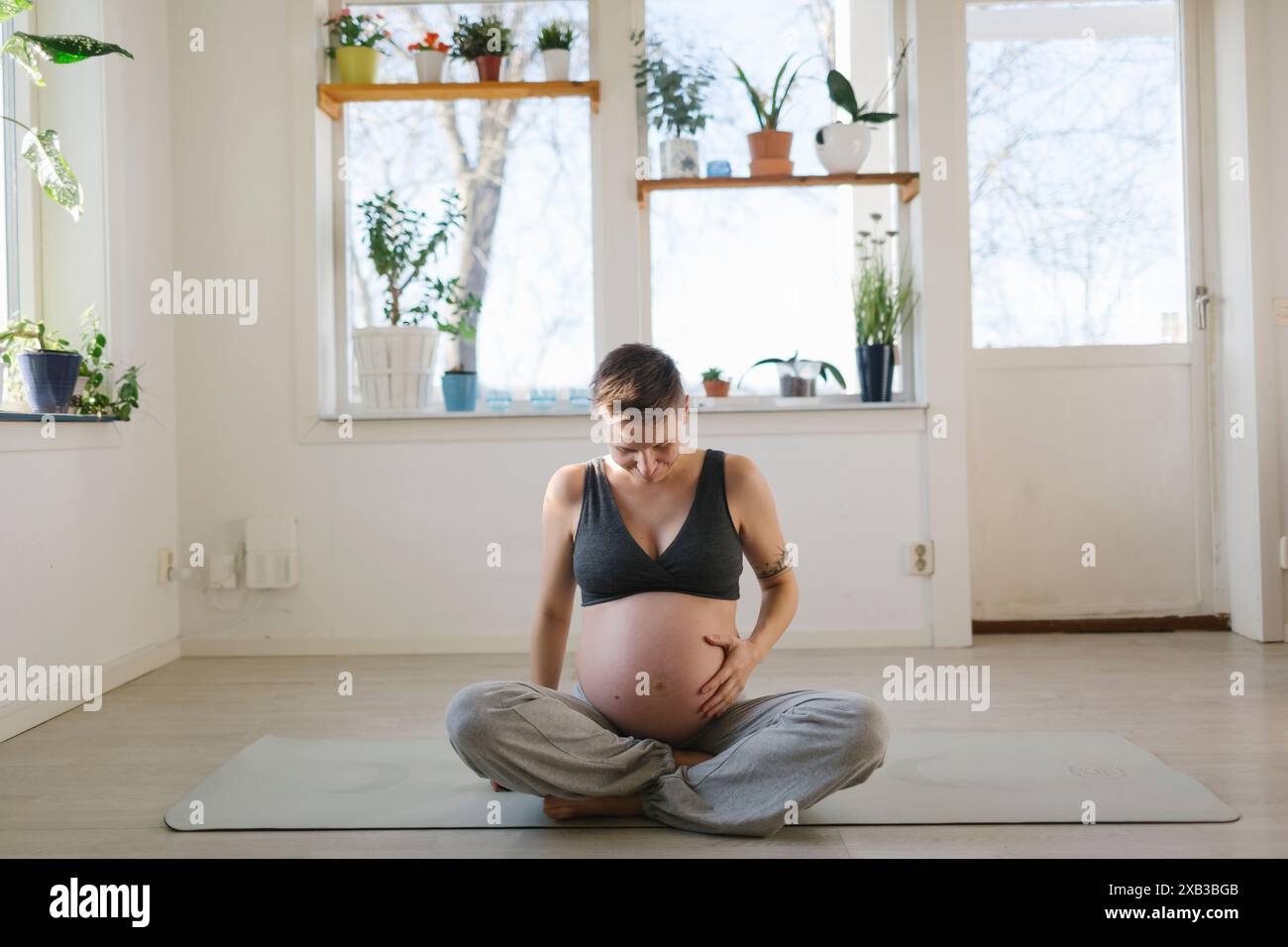 Jeune femme enceinte touchant l'abdomen tout en étant assise sur un tapis d'exercice à la maison Banque D'Images