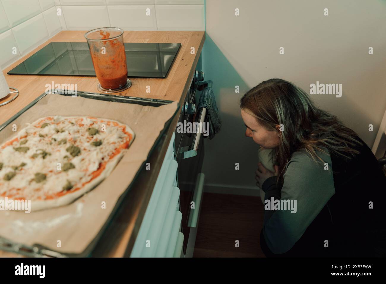 Vue en angle élevé de la jeune femme accroupie tout en regardant le four sous le comptoir de cuisine à la maison Banque D'Images