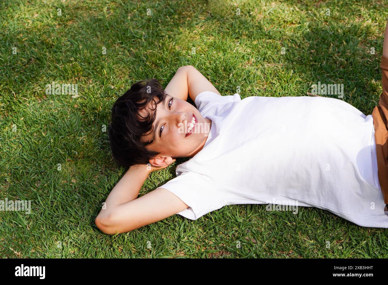 garçon pré-adolescent souriant allongé sur l'herbe avec ses bras derrière la tête, détendu et insouciant. Banque D'Images