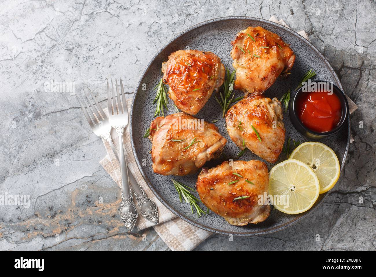 Cuisses de poulet marinées puis cuites au four avec citron et romarin servies avec ketchup gros plan dans une assiette sur la table. Vue horizontale de dessus Banque D'Images