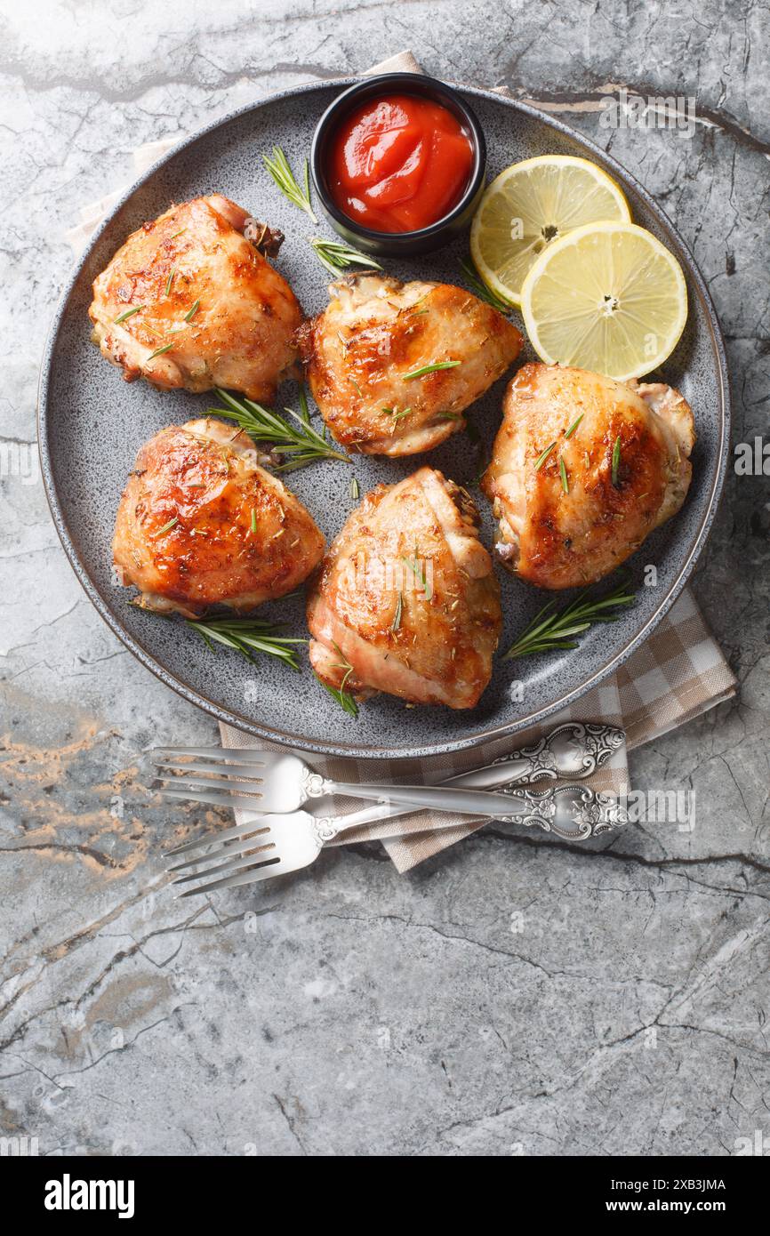 Cuisses de poulet cuites au romarin, jus de citron et zeste gros plan dans une assiette sur la table. Vue de dessus verticale Banque D'Images