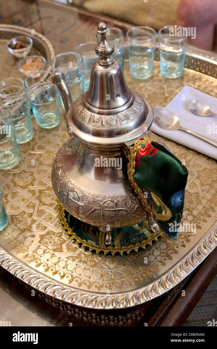 Théière de cérémonie marocaine polie avec décoration traditionnelle, couvercle de poignée, support de théière et verres debout sur un plateau de service en argent embelli. Banque D'Images Théière de cérémonie marocaine polie avec décoration traditionnelle, couvercle de poignée, support de théière et verres debout sur un plateau de service en argent embelli. Banque D'Images