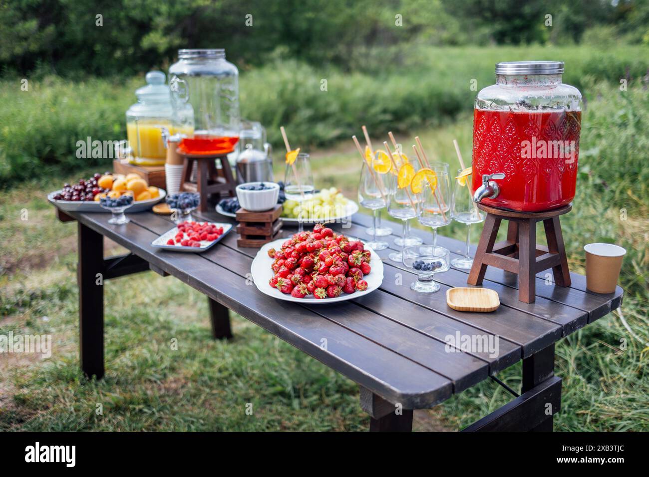 Une table en bois avec des baies et des fruits sucrés, des pots de jus fraîchement pressé et des verres vides. Un buffet d'été en plein air. Délicieux en-cas aux fruits Banque D'Images