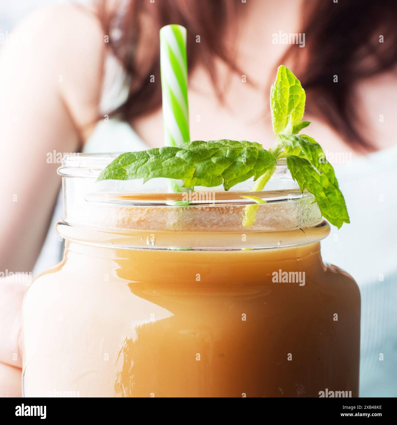 Une jeune fille tient une tasse en verre avec du jus dans la main. Jus frais à la menthe. Mise au point sélective Banque D'Images Une jeune fille tient une tasse en verre avec du jus dans la main. Jus frais à la menthe. Mise au point sélective Banque D'Images