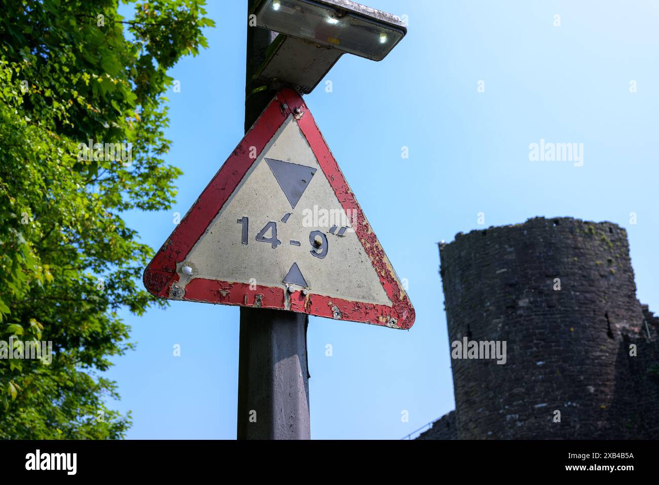 Conwy Wales UK 06-01-2024. Vieux panneau triangulaire de restriction de hauteur par tour de pierre sous ciel bleu vif Banque D'Images
