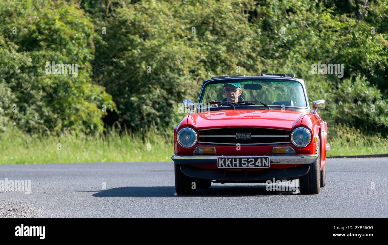 Stony Stratford, Royaume-Uni - 2 juin 2024 : 1975 Red Triumph TR6 voiture classique conduisant sur une route de campagne britannique Banque D'Images