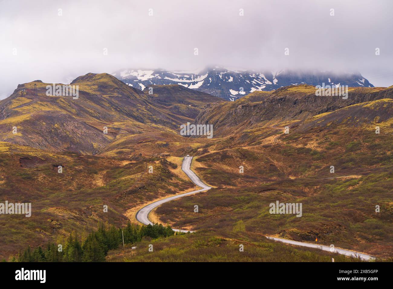 Route à travers un paysage volcanique de l'Islande, vue aérienne, neige inégale, herbe jaune, ciel nuageux. Banque D'Images