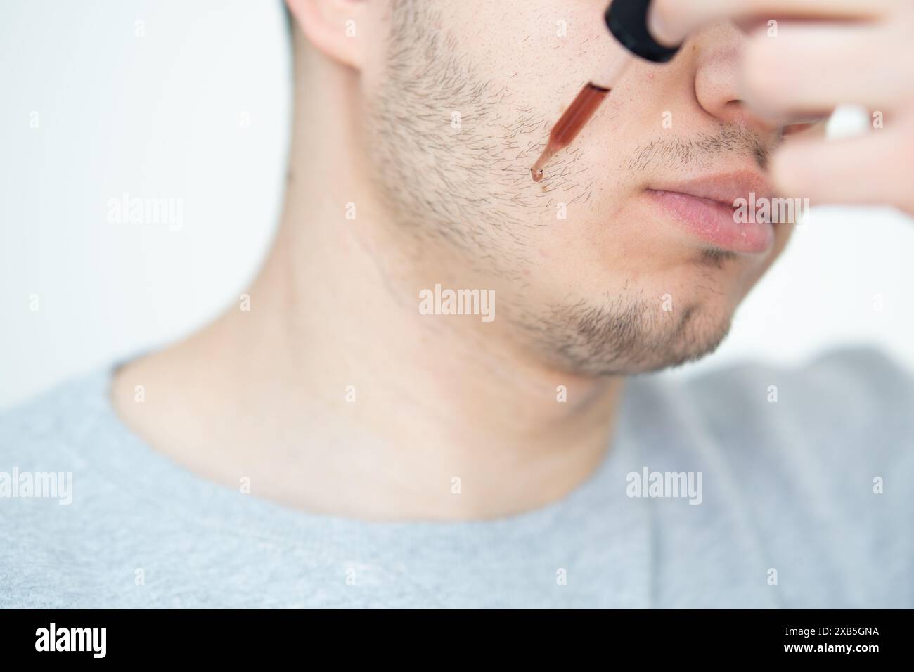 jeune homme appliquant l'huile de croissance de barbe avec pipette gros plan. homme tenant la pipette avec de l'huile pour la barbe, appliquant le sérum cosmétique avec la pipette sur le visage Banque D'Images