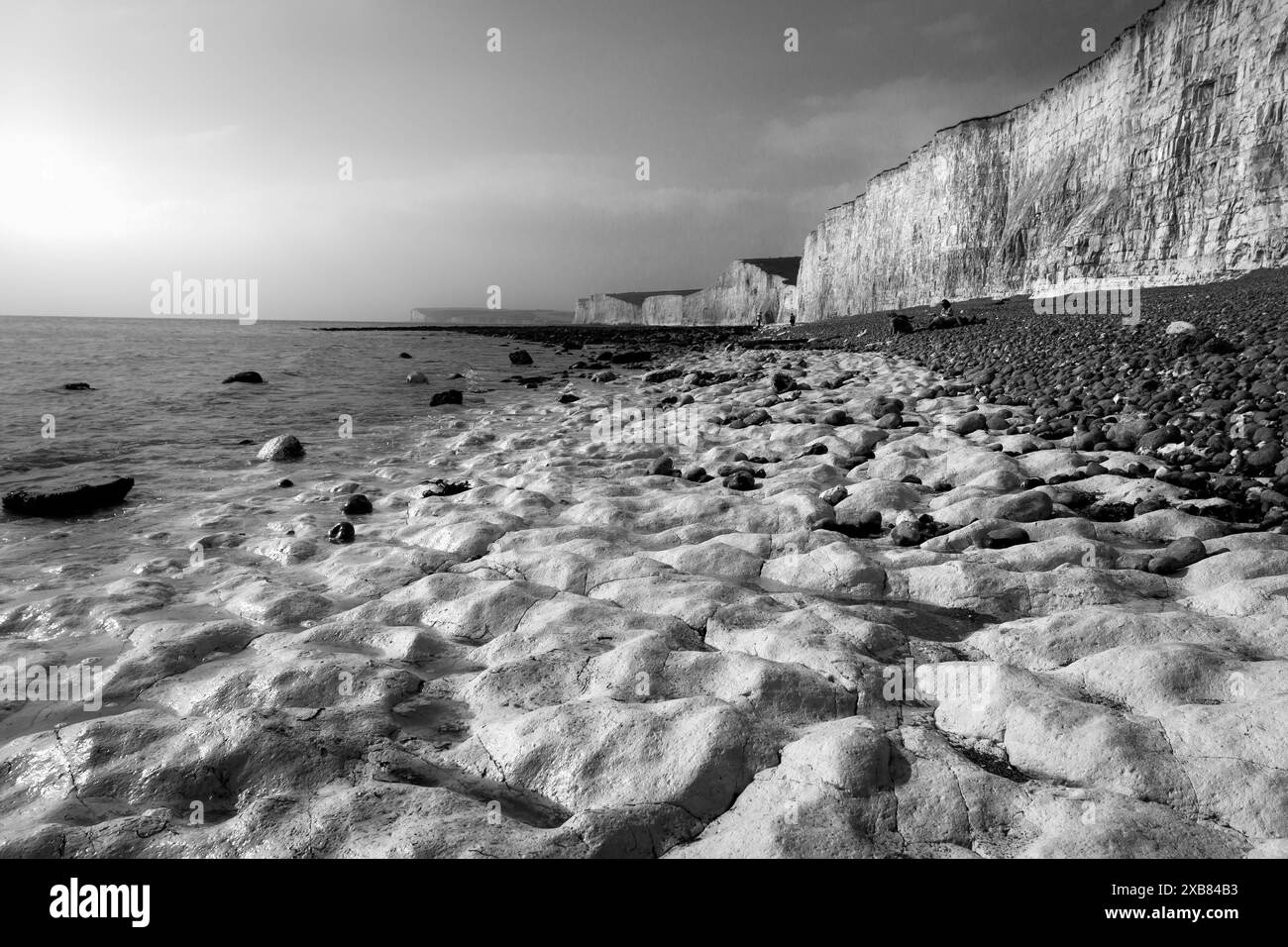 Un homme se tient sur une plage rocheuse au bord de l'eau, près des falaises Banque D'Images