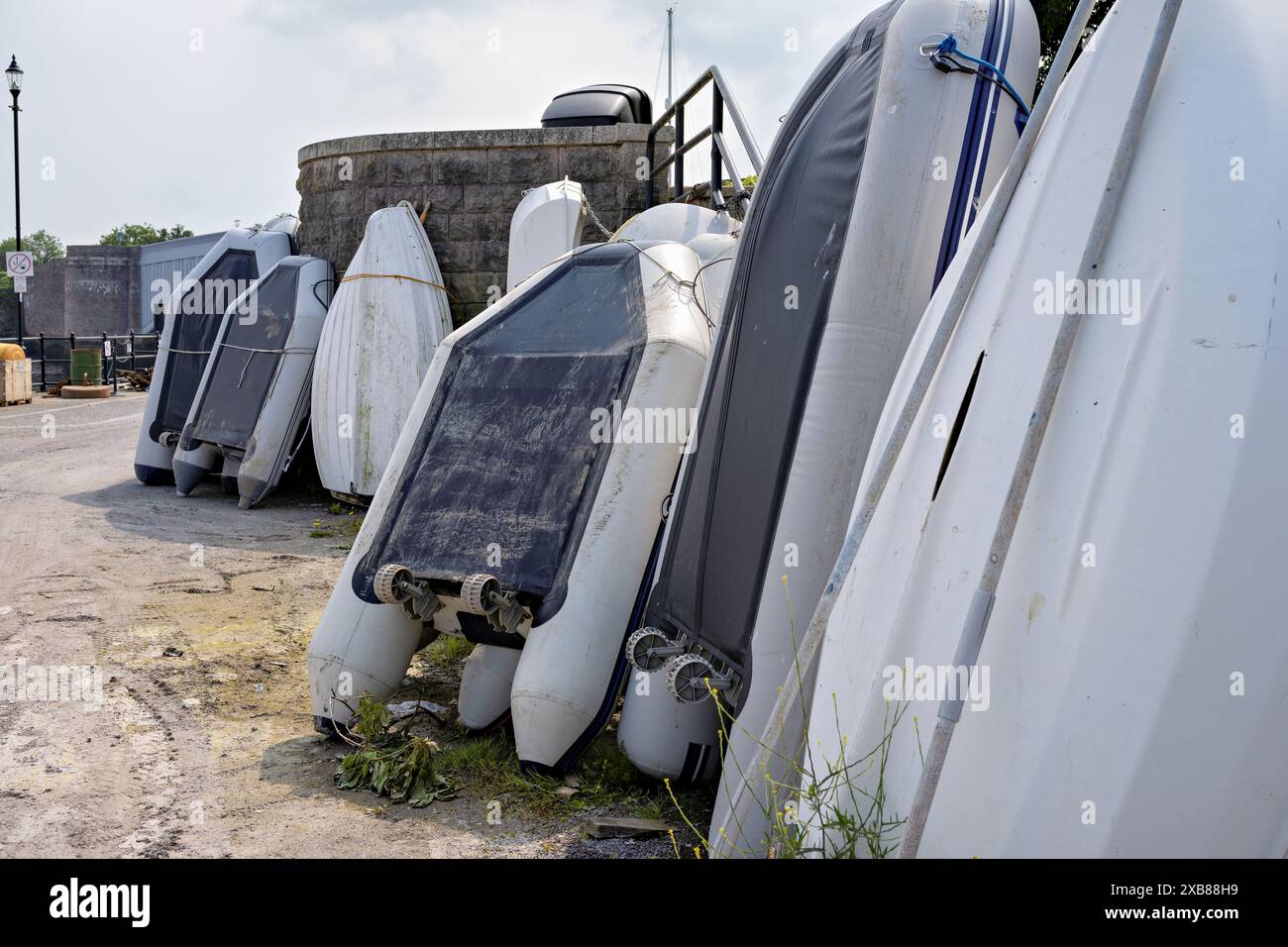Canots gonflables renversés et petits bateaux sur quai de béton, prêts pour la réparation ou le stockage par l'accès au bateau de marina. Banque D'Images