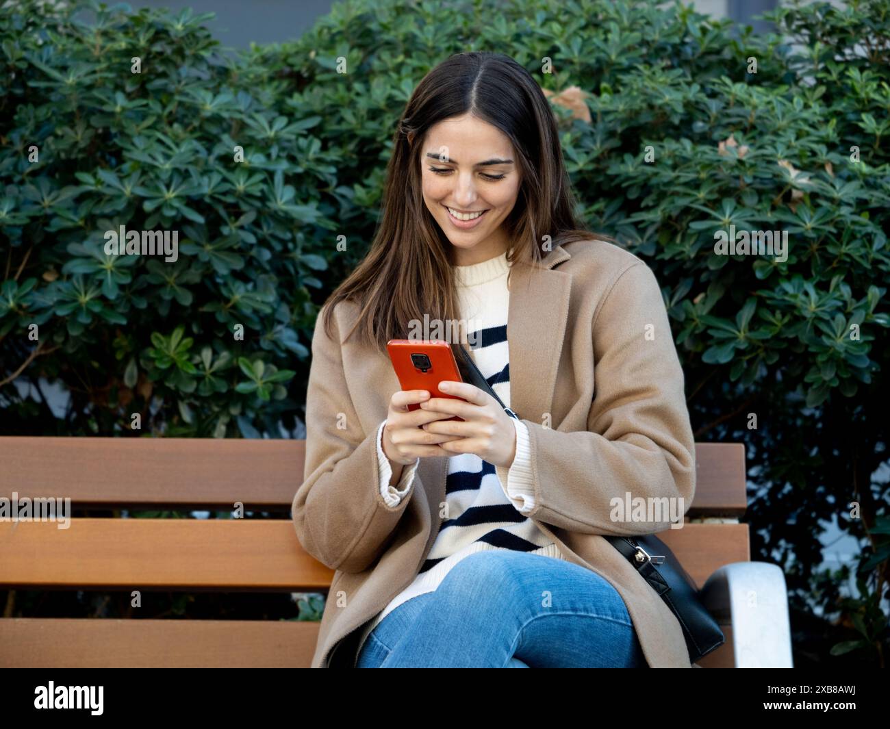 Élégante jeune femme assise sur un banc dans une ville discutant avec un smartphone Banque D'Images