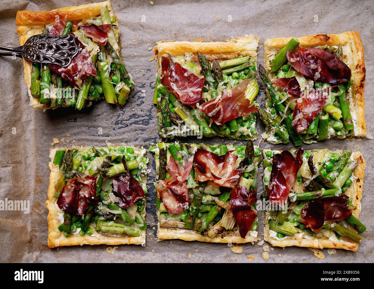 Ces photos présentent une tarte à pâte feuilletée cuite au four garnie d'asperges vertes éclatantes, de petits pois, de fromage râpé et de fines tranches de jambon séché. La tarte est coupée Banque D'Images