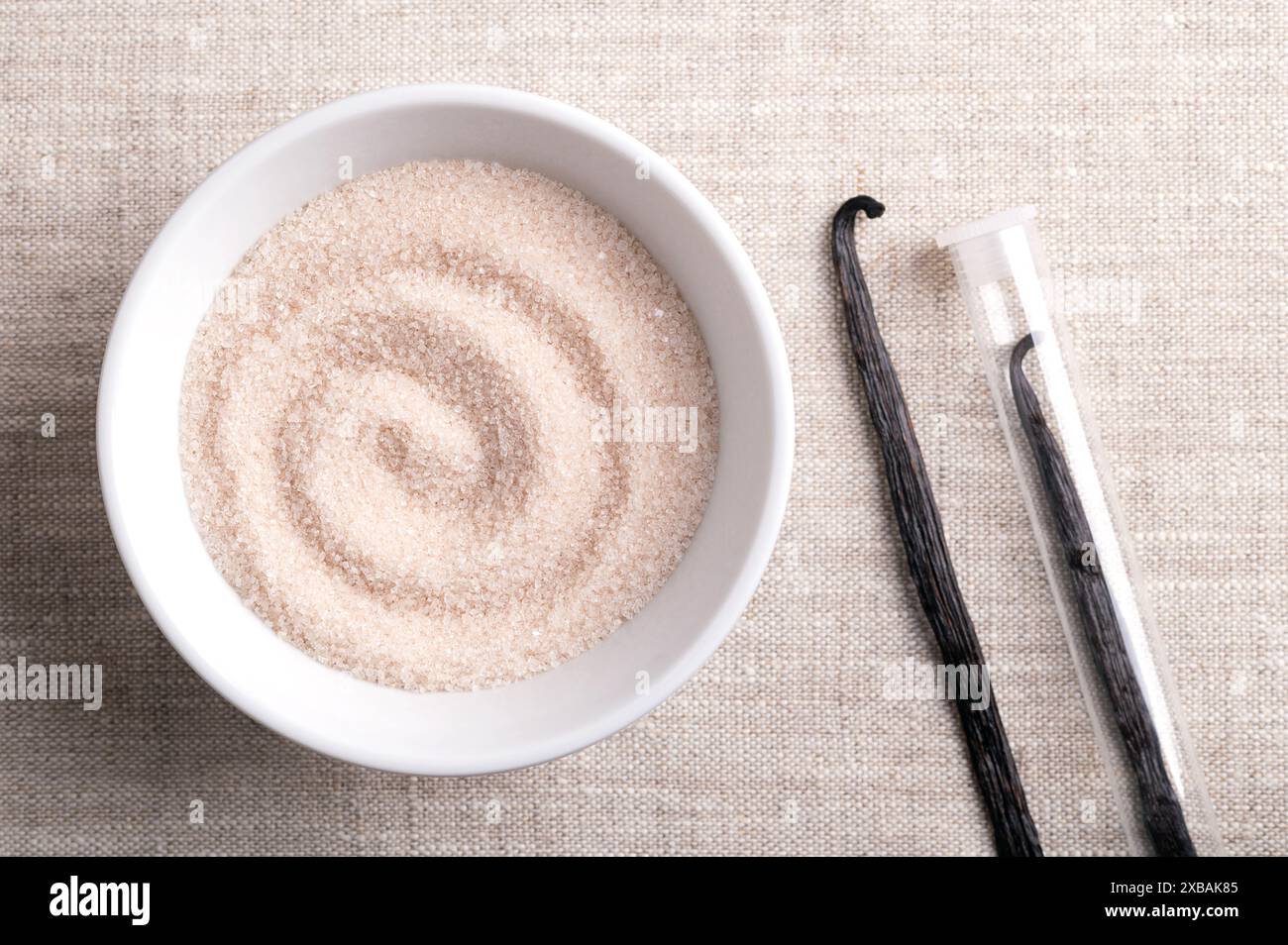 Sucre vanillé, sucre aromatisé dans un bol blanc sur tissu de lin, à côté de gousses séchées, brunes, mûres ou haricots de Vanilla planifolia, une épice. Banque D'Images