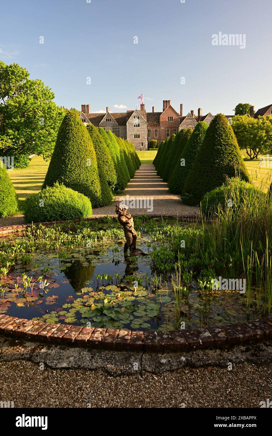 Étang de nénuphars ornementaux et haies coniques dans le jardin arrière de Littlecote House, un hôtel Warner dans le Wiltshire, vu dans le soleil de fin de soirée. Banque D'Images