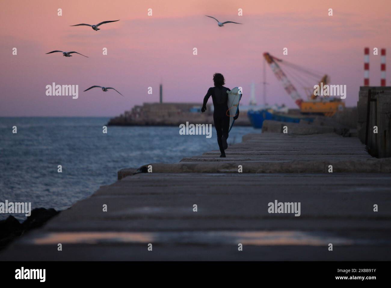 surfeur courant le long de la jetée juste après le coucher du soleil avec le port et l'océan en arrière-plan Banque D'Images