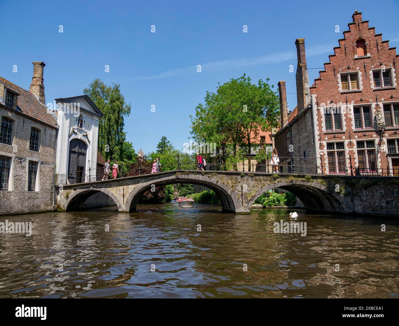 Pont historique sur une rivière, bordée de vieux bâtiments et d'arbres, sous un ciel dégagé, Bruges, Flandre, Belgique Banque D'Images