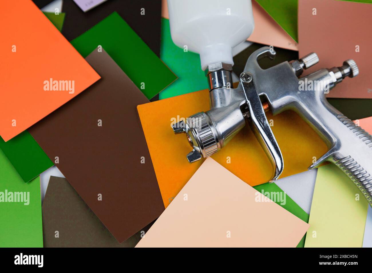 un pistolet à peinture au travail sur le lieu de travail dans l'atelier. Échantillons de peinture Banque D'Images un pistolet à peinture au travail sur le lieu de travail dans l'atelier. Échantillons de peinture Banque D'Images