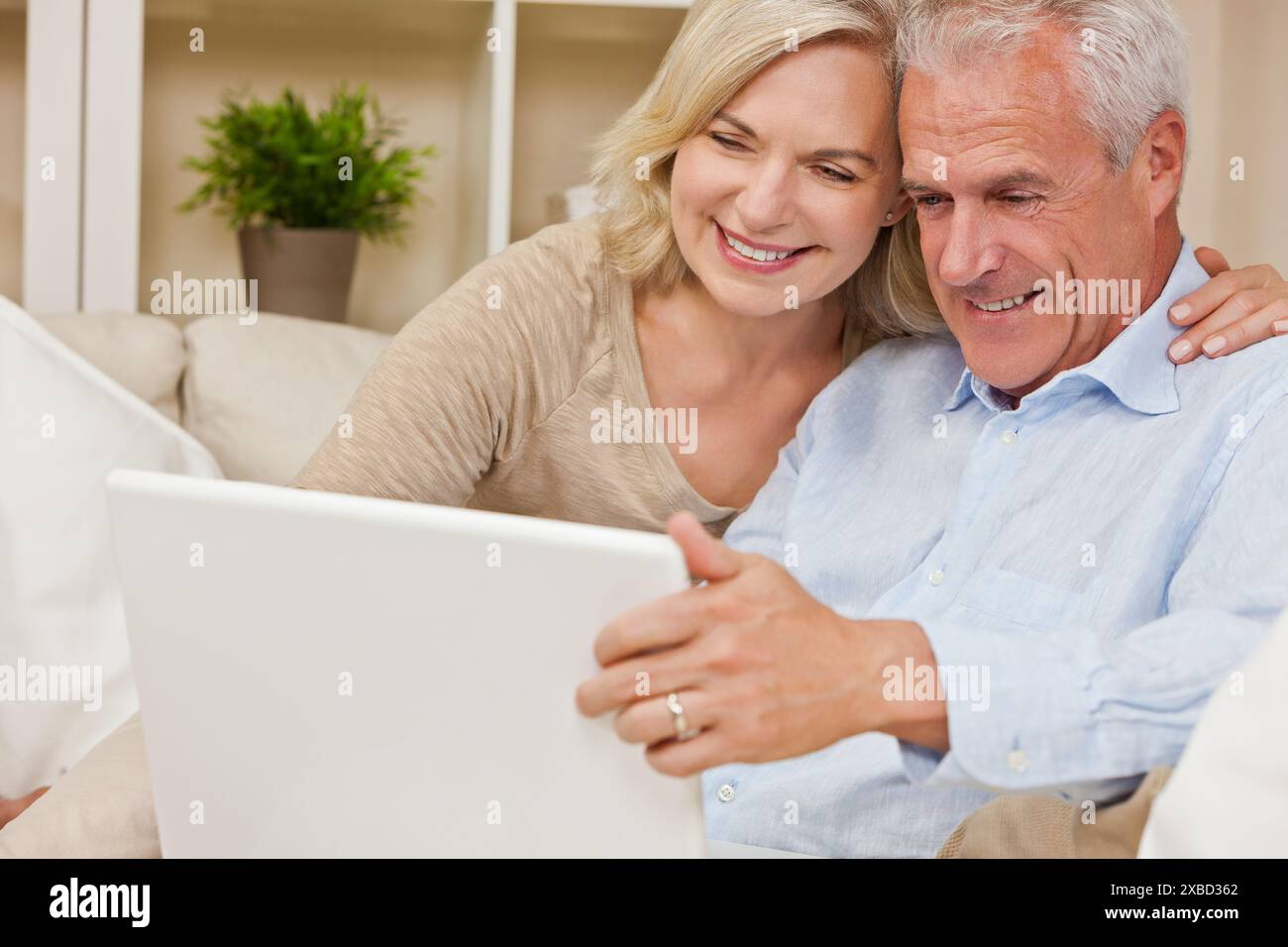 Heureux homme senior et couple de femme assis ensemble à la maison souriant et heureux à l'aide d'un ordinateur portable Banque D'Images