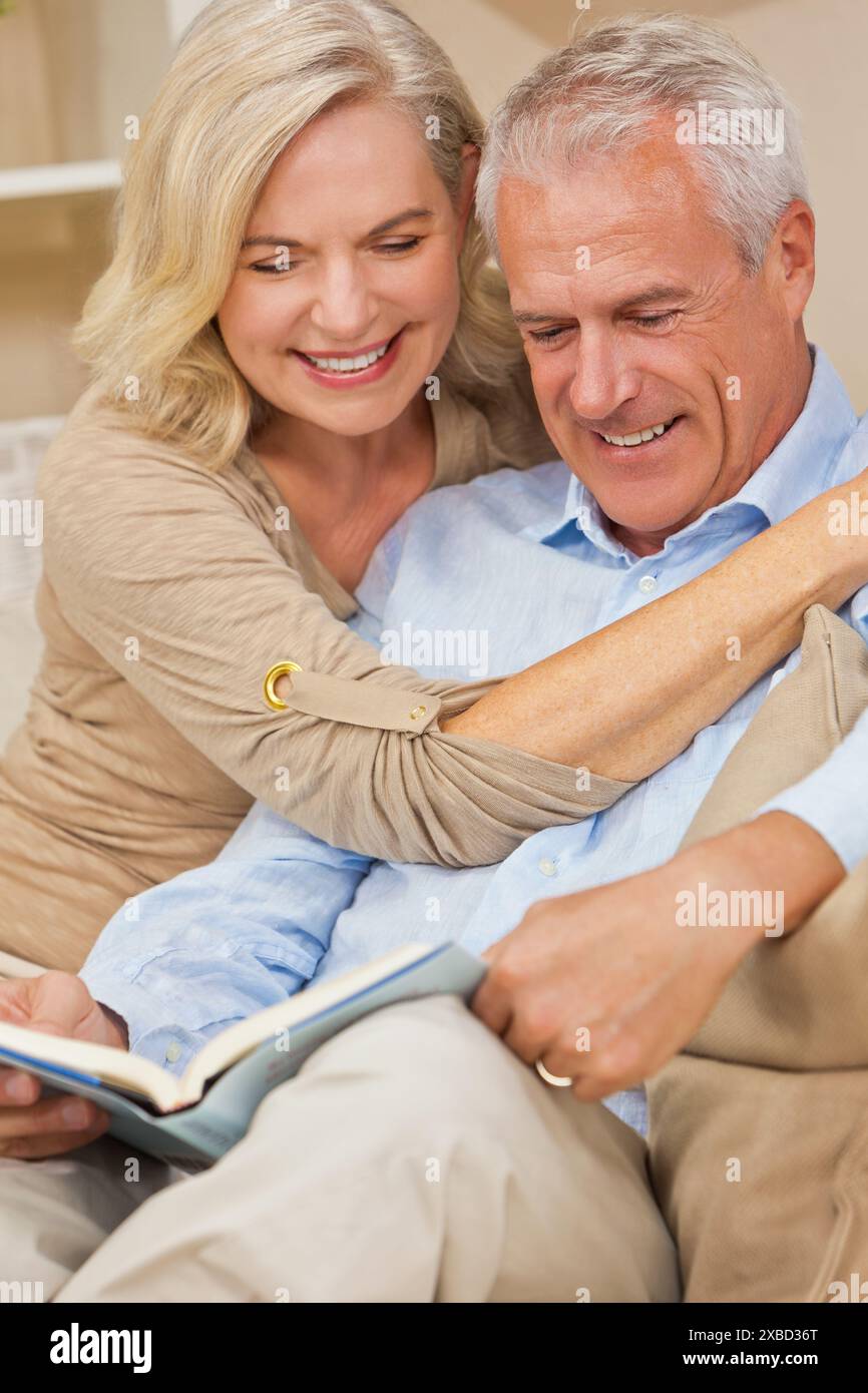 Attrayant couple de femmes âgées en bonne santé à la maison souriant lisant un livre Banque D'Images