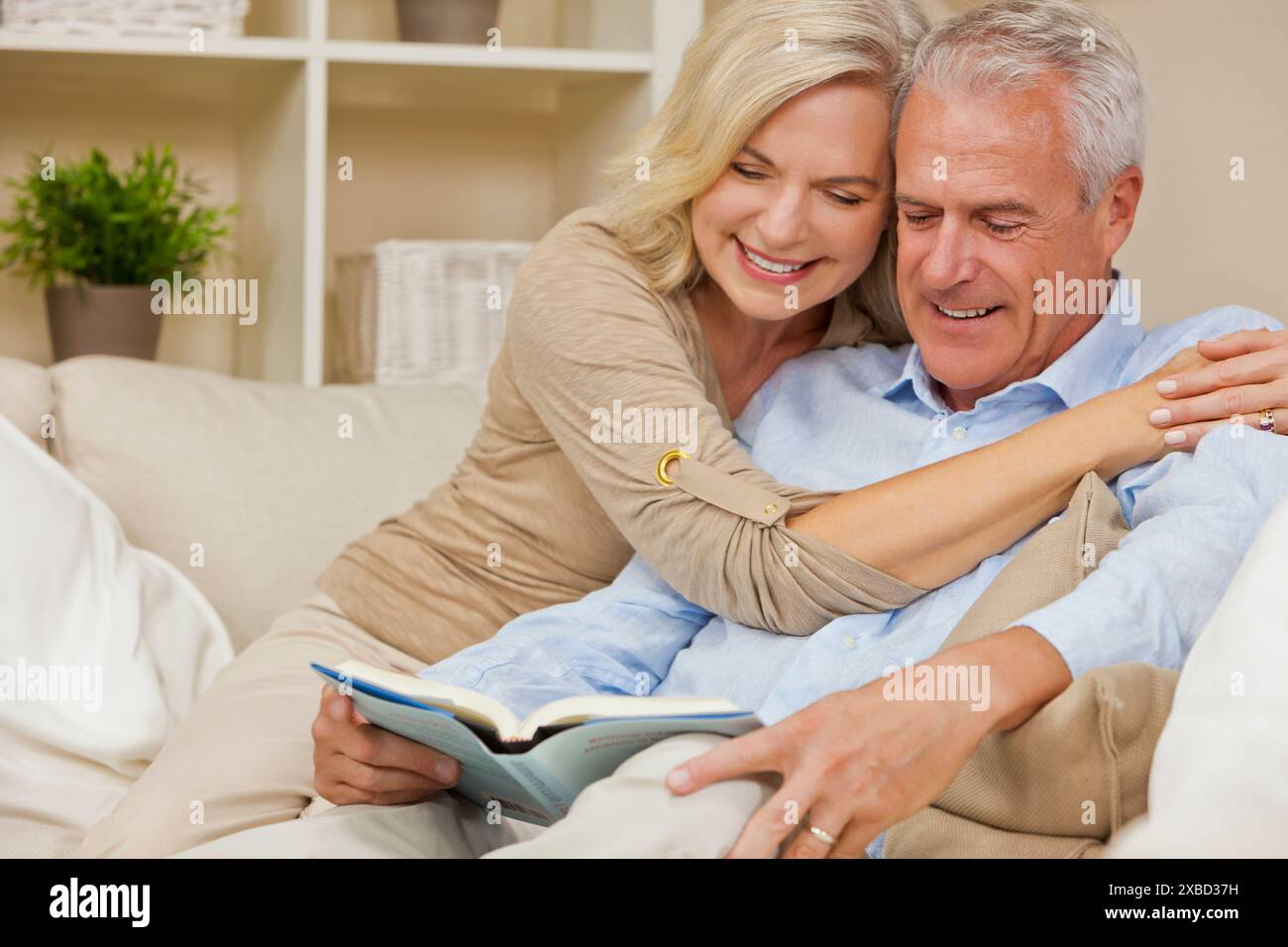 Attrayant couple de femme Senior en bonne santé à la maison souriant lecture d'un livre Banque D'Images