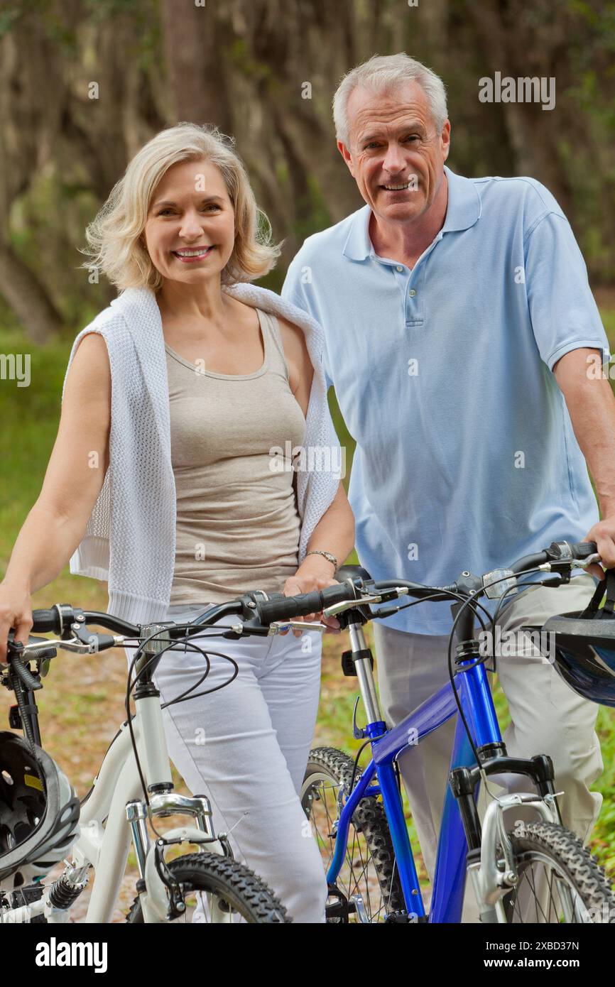 Heureux homme senior et femme retraité couple ensemble souriant à vélo sur des vélos dans un parc Banque D'Images
