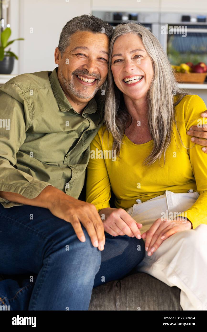 Un couple biracial mature est assis ensemble, souriant chaleureusement à la caméra, à la maison Banque D'Images