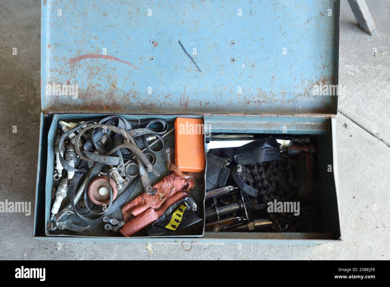 Une vieille boîte à outils en métal, couvercle ouvert, son contenu comprend des pièces de bicyclette, une bougie d'évier et une languette de feuille Polaroid, une pédale, caoutchouc de jante, bougies d'allumage, kit de patch Banque D'Images