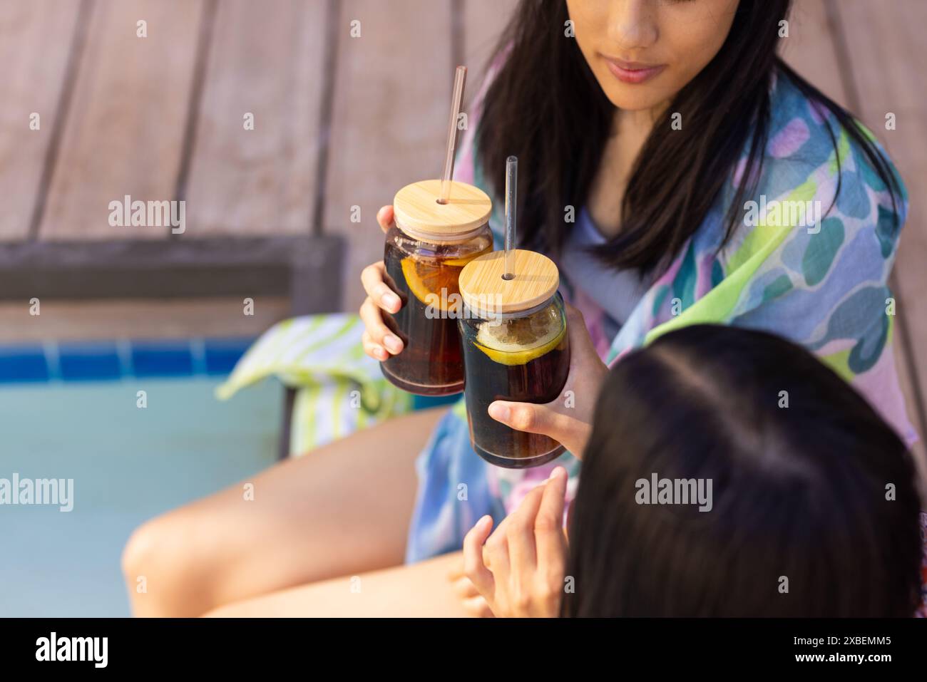 Deux jeunes sœurs biraciales prenant un verre ensemble au bord de la piscine, à la maison Banque D'Images