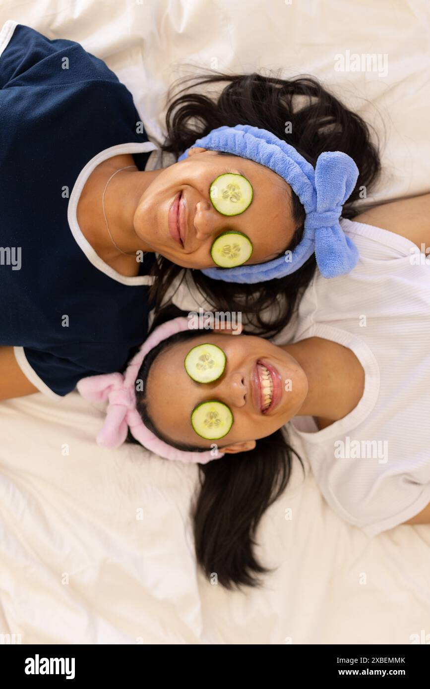 Deux jeunes sœurs biraciales se relaxant avec des tranches de concombre sur les yeux, à la maison Banque D'Images