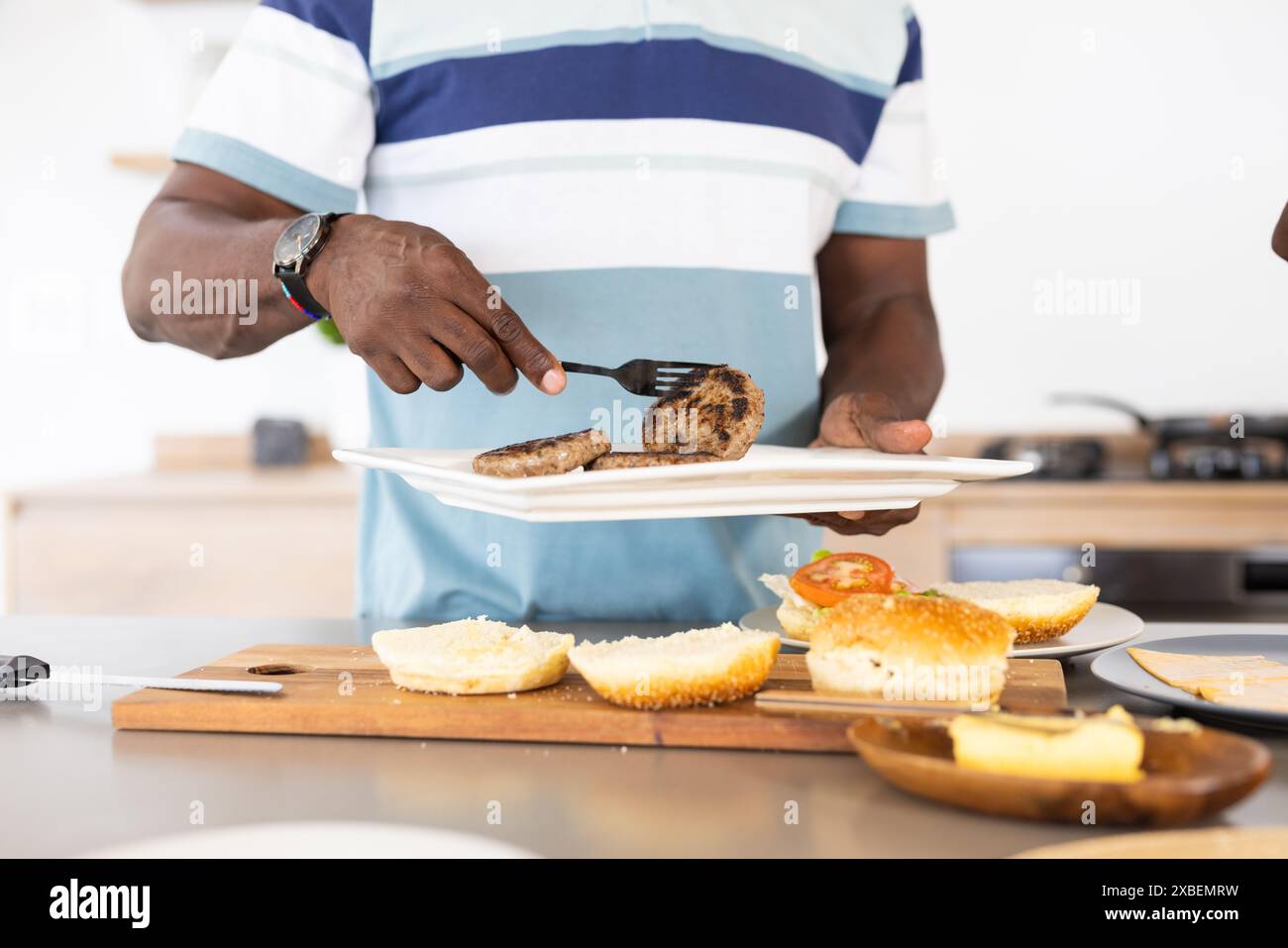 Homme afro-américain mature griller des hamburgers dans la cuisine moderne Banque D'Images