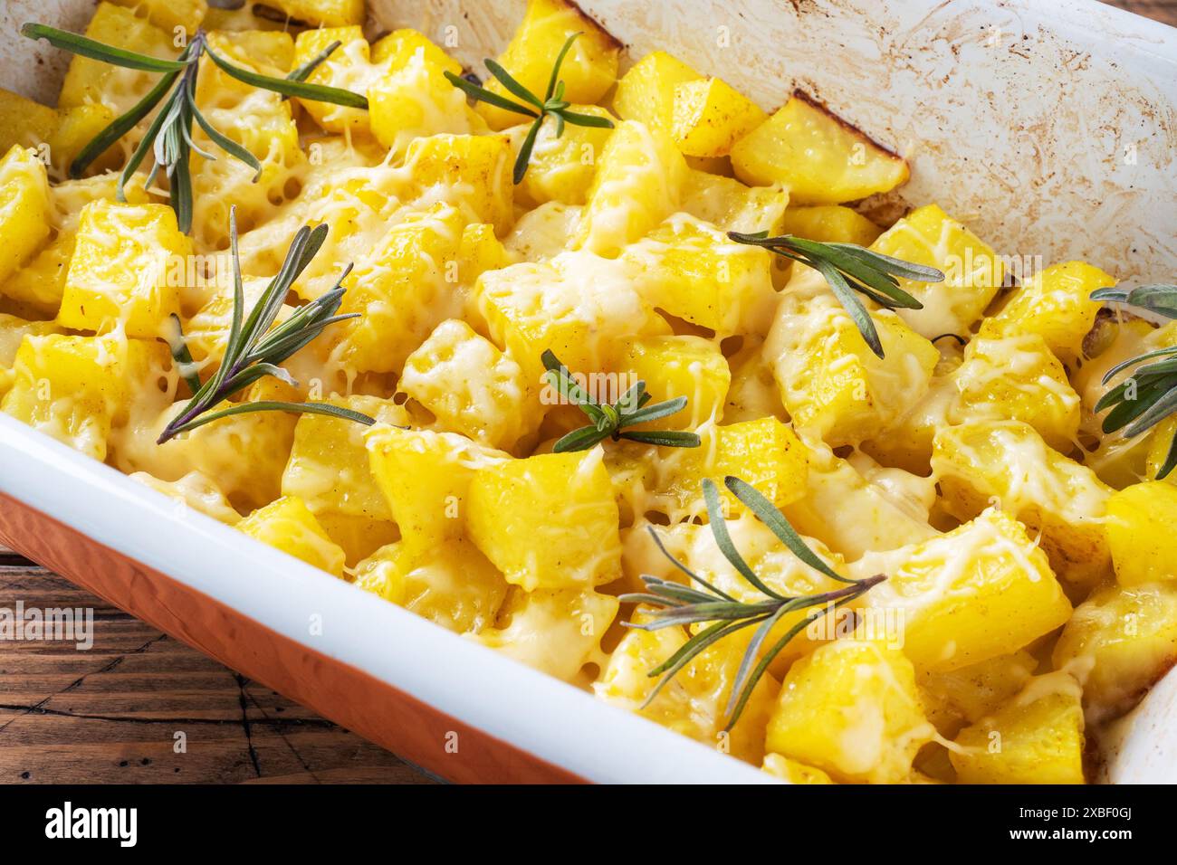 Délicieuses pommes de terre cuites au four avec des épices fromage et romarin dans une plaque de cuisson en céramique sur un fond rustique en bois de gros plan Banque D'Images Délicieuses pommes de terre cuites au four avec des épices fromage et romarin dans une plaque de cuisson en céramique sur un fond rustique en bois de gros plan Banque D'Images